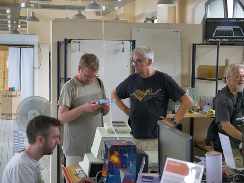 Vier Männer in einem technischen Arbeitsraum mit alten Computern und Retro-Geräten.