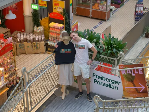 Mann im Retro-T-Shirt posiert neben Schaufensterpuppe im Einkaufszentrum bei Marktständen.