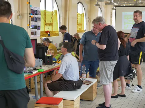 Menschen bei einem interaktiven Tech-Workshop mit Computern und Elektronik in einer hellen Halle.