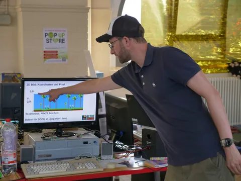 Mann in Baseballkappe zeigt auf Computermonitor mit Pixelgrafik-Software