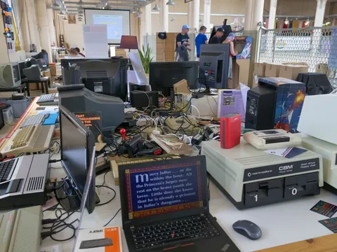 Retro-Computer-Ausstellung mit alten Monitoren, Commodore-Hardware und Laptop mit Text auf dem Bildschirm.