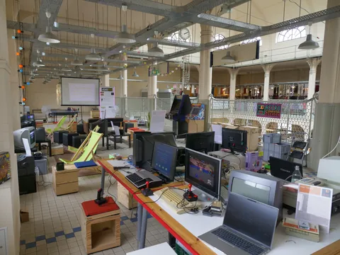 Retro-Computer-Ausstellung mit alten PCs, Monitoren, Joysticks und Arcade-Automaten in einer großen Halle.