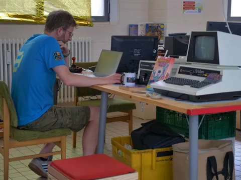 Mann im blauen T-Shirt arbeitet an Laptop neben Retro-Computern wie Commodore CBM.