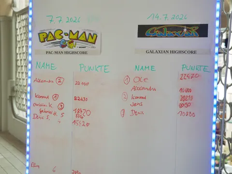 Whiteboard mit Pac-Man und Galaxian Highscores, handgeschriebenen Spielernamen und Punktzahlen.