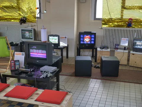 Retro-Gaming-Raum mit mehreren CRT-Monitoren, alten Videospielkonsolen und Spielzubehör.