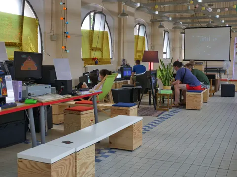 Menschen arbeiten an Computern in einem hellen Raum mit hohen Fenstern und Holzmoebeln.