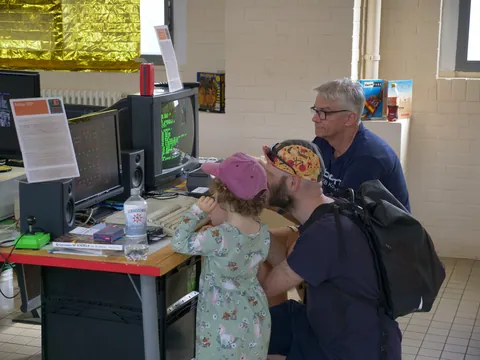 Zwei Männer und ein Mädchen betrachten Retro-Computer mit grünem Text auf dem Bildschirm.