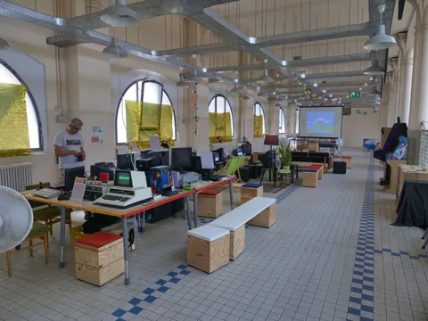 Großer Raum mit Vintage-Computern auf Tischen, Mann arbeitet daran, hohe Rundbogenfenster und Industriedecke.