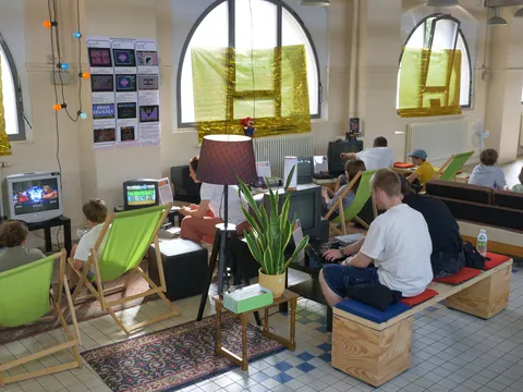 Menschen spielen Videospiele an alten Fernsehern in einem Raum mit großen Bogenfenstern.