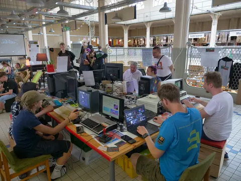 Menschen arbeiten und spielen an Retro-Computern mit Röhrenmonitoren in einer großen Veranstaltungshalle.