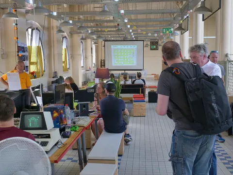 Teilnehmer mit Computern und Projektor in einem hellen Workshop- oder Veranstaltungsraum.