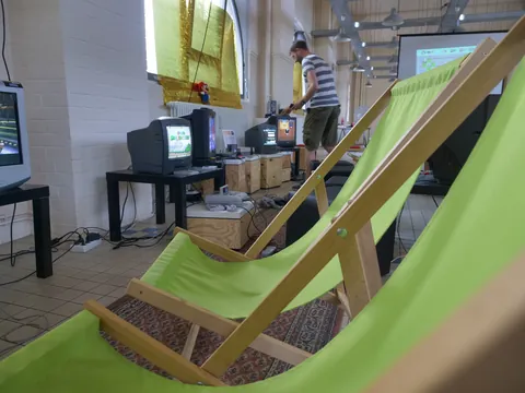 Grüne Liegestühle im Vordergrund, Mann zwischen mehreren alten Computermonitoren im Hintergrund.