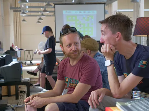 Teilnehmer einer Retro-Computer-Veranstaltung sitzen vor alten Computern mit Beamer im Hintergrund.