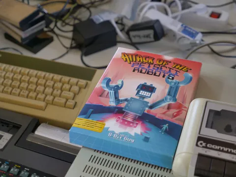 Spielbox „Attack of the PETSCII Robots“ auf Schreibtisch mit Retro-Computern.