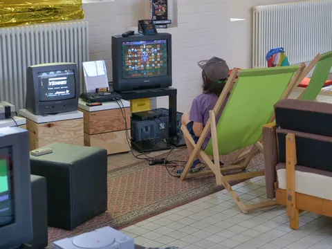 Kind spielt Videospiel auf altem Sony-Fernseher umgeben von Retro-Computern im Wohnzimmer.