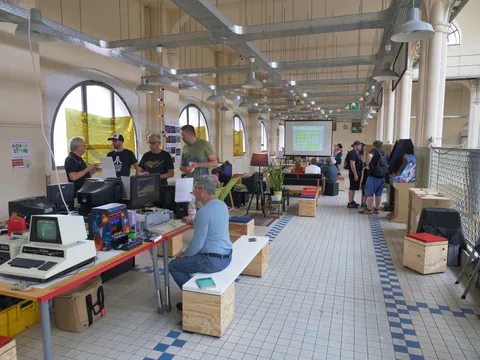 Retro-Computing-Veranstaltung in einer Halle mit vintage Computern, Arcade-Spielen und Besuchern.