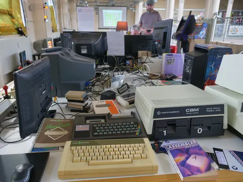 Schreibtisch voller alter Computer, darunter Commodore-Geräte, CRT-Monitore und Handbücher.