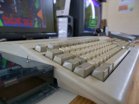 Retro-Computerarbeitsplatz mit beigem Keyboard, Diskettenlaufwerk und zwei Monitoren im Hintergrund.