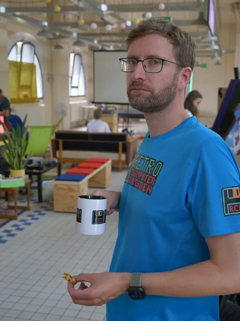 Mann mit Brille und Bart in blauem T-Shirt hält Tasse und Keks.