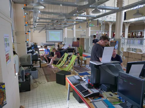 Mehrere Personen nutzen alte Computermonitore in einem großen Raum mit Beamer und Deckchairs.