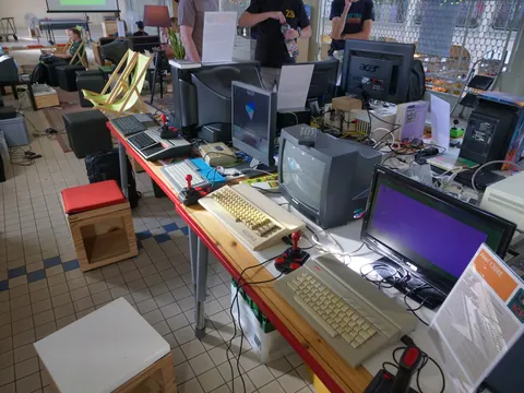 Tisch voller Retro-Computer, alter Monitore, Tastaturen und Joysticks bei einer Ausstellung.