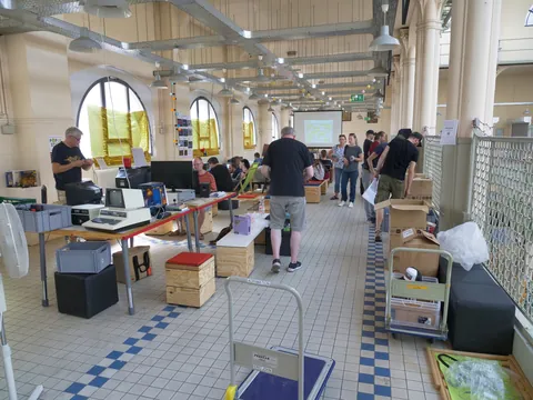 Menschen betrachten alte Computer und Retro-Technik auf Tischen in einer großen, hellen Halle.