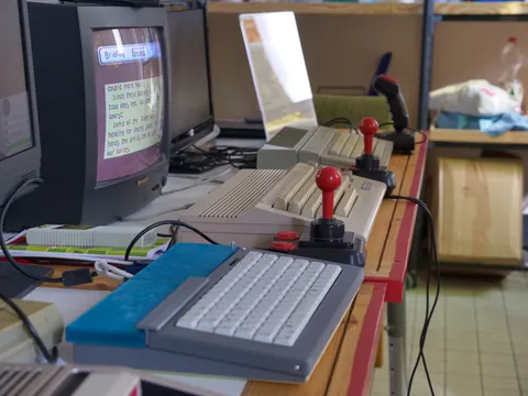 Vintage-Computer mit Röhrenmonitor, Tastaturen und roten Joysticks auf einem Holztisch.
