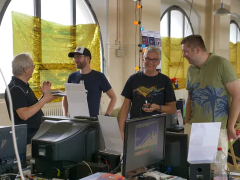 Vier Männer diskutieren vor Retro-Computern in einem Workshop mit goldener Fensterfolie.