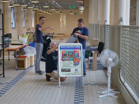 Drei Männer richten in einer Markthalle ein Schild für die Retro Computer Lounge auf.