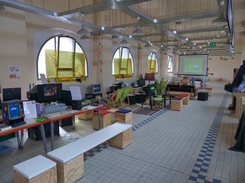 Geräumige Retro-Gaming-Lounge mit Computertischen, Liegestühlen, hohen Rundfenstern und Beamer-Leinwand.