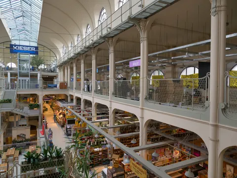 Historische Markthalle mit mehreren Etagen, Glasdach und Geschäften im Erdgeschoss.