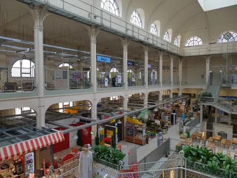 Historische zweistöckige Markthalle mit Arkadengang, weißen Pfeilern, Rundfenstern und Einzelhandel.