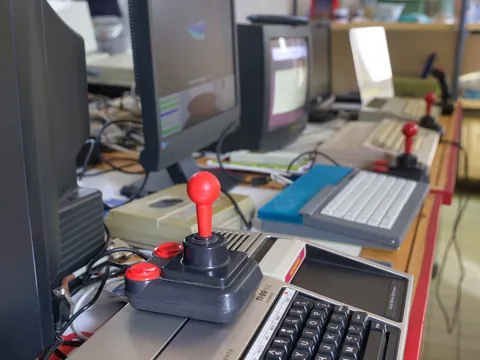 Roter Joystick auf einem Retrocomputer zwischen alten Monitoren und Tastaturen auf einem Schreibtisch.