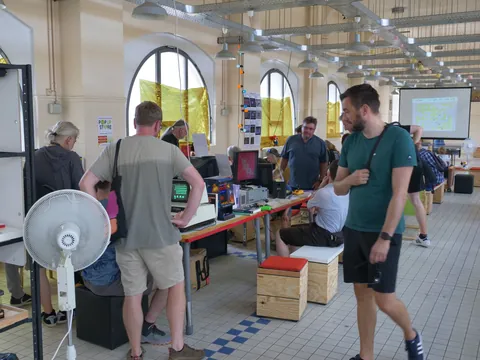 Menschen in einem Workshop-Raum mit Retro-Computern und Elektronik an Tischen.