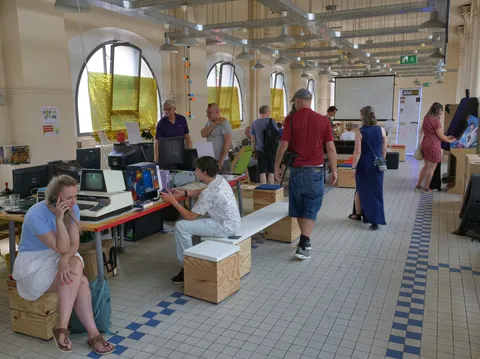 Besucher betrachten Vintage-Computer und Retro-Geräte in einer hellen Ausstellungshalle mit hohen Fenstern.