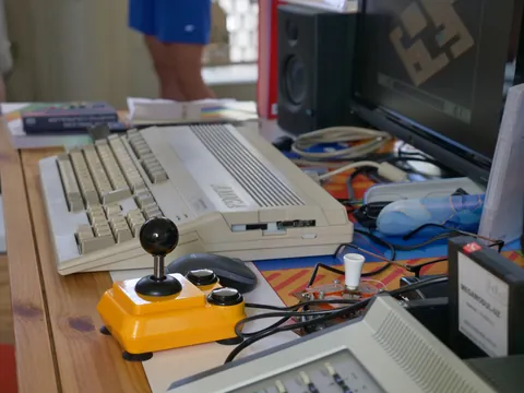 Vintage Amiga Computer mit gelbem Joystick und Peripheriegeräten auf einem Holzschreibtisch.