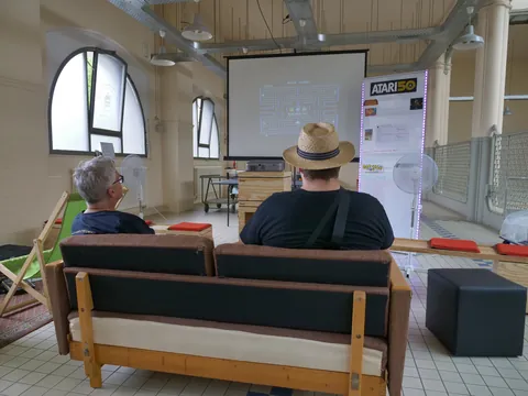 Zwei Personen auf einem Sofa vor einer Projektionswand bei einer Atari-Veranstaltung.