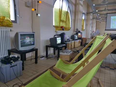 Retro-Gaming-Raum mit mehreren CRT-Fernsehern, grünen Liegestühlen und goldenen Fenstervorhängen.