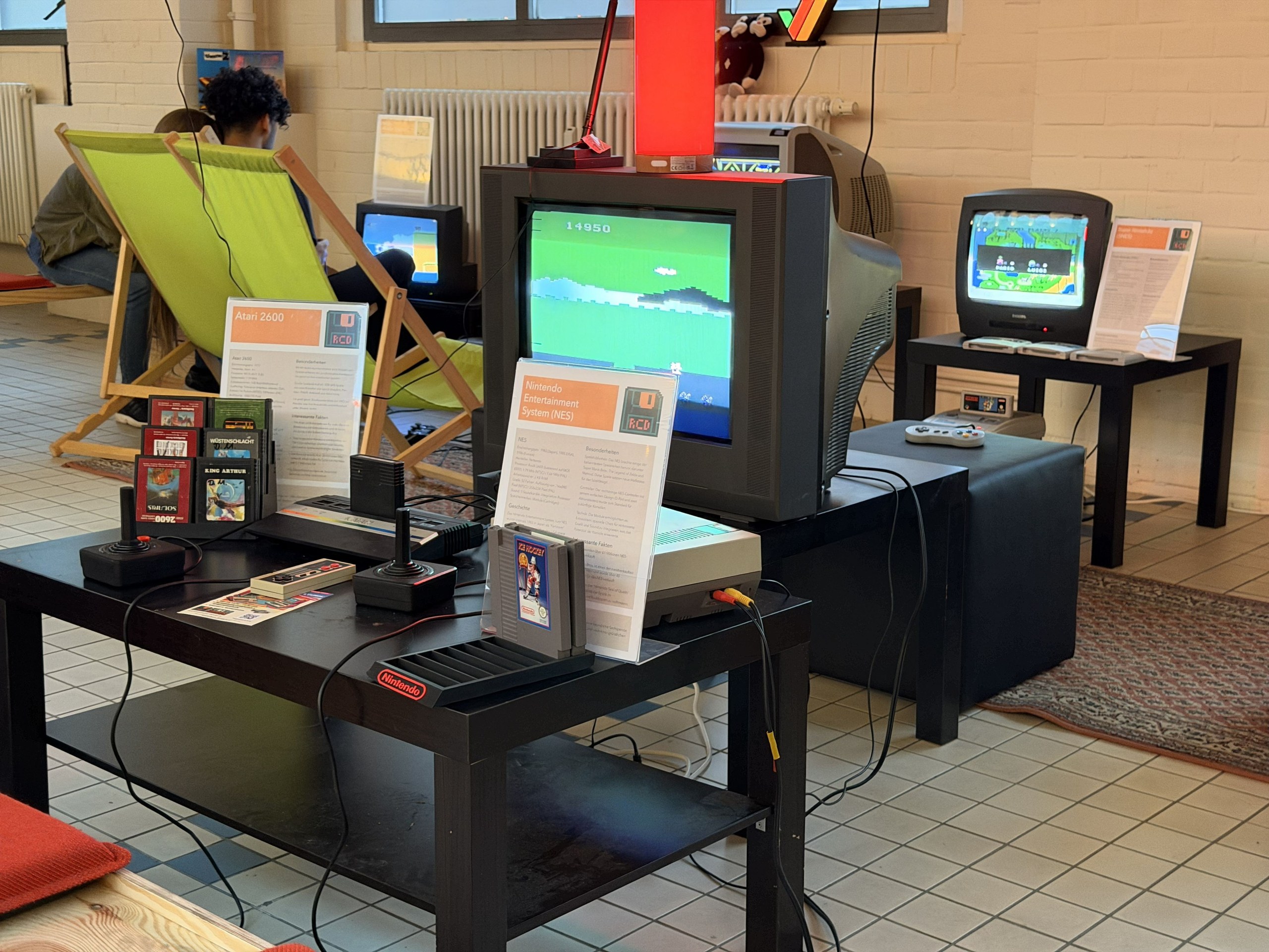 Ausstellungstisch mit Atari 2600 und NES samt Infotafeln und Modulsammlung